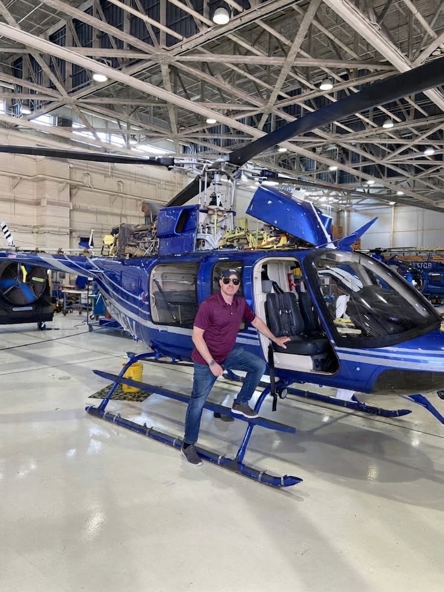 Ennesser Aviation FAA Part 107 certified drone pilot with DEA law enforcement background posing with a helicopter in an aviation hangar